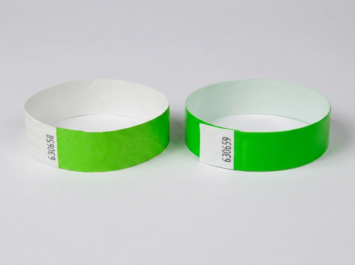 Confronto affiancato di un braccialetto Tyvek bianco con codice a barre stampato e di un braccialetto identificativo colorato con codice a barre, posati su un tavolo di festival